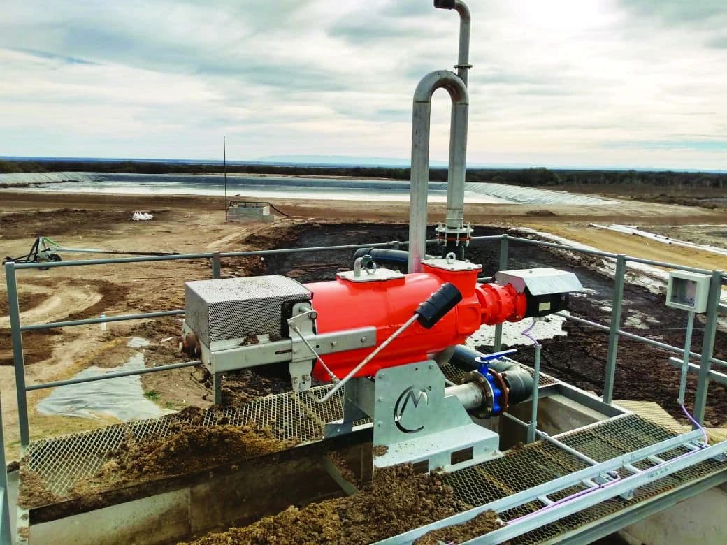 A large, orange CRI-MAN wastewater treatment pump installed at an outdoor processing plant. The pump is
positioned over a channel containing wastewater, with a wide, open landscape and settling ponds visible in the background, illustrating its use in a real-world
application.